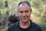 The writer Kim Scott standing in front of the Australian bush, looking concerned