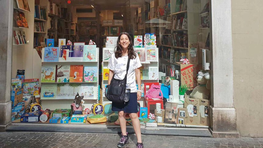 Lara stands in front of a bookshop window filled with books