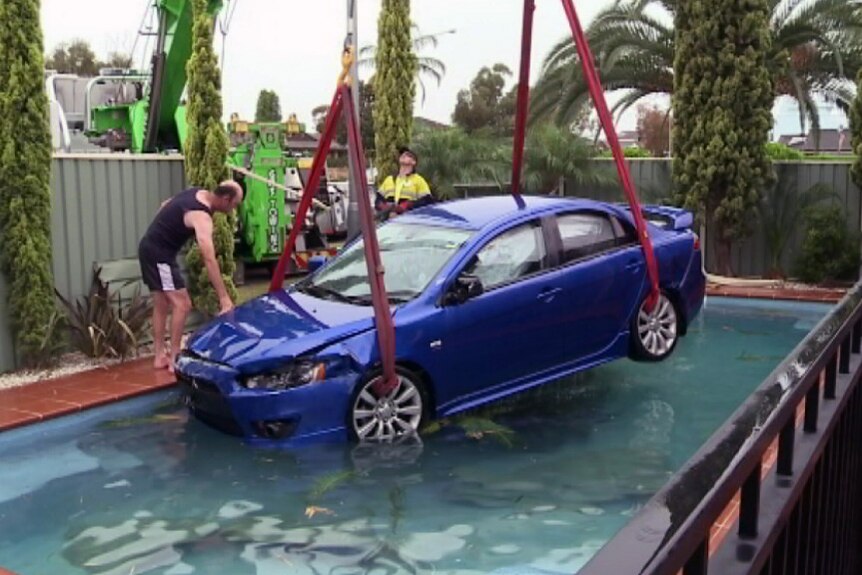 A car is winched out of a backyard pool
