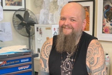 Artist Benny Blackbird sits in a tattoo parlour and smiles