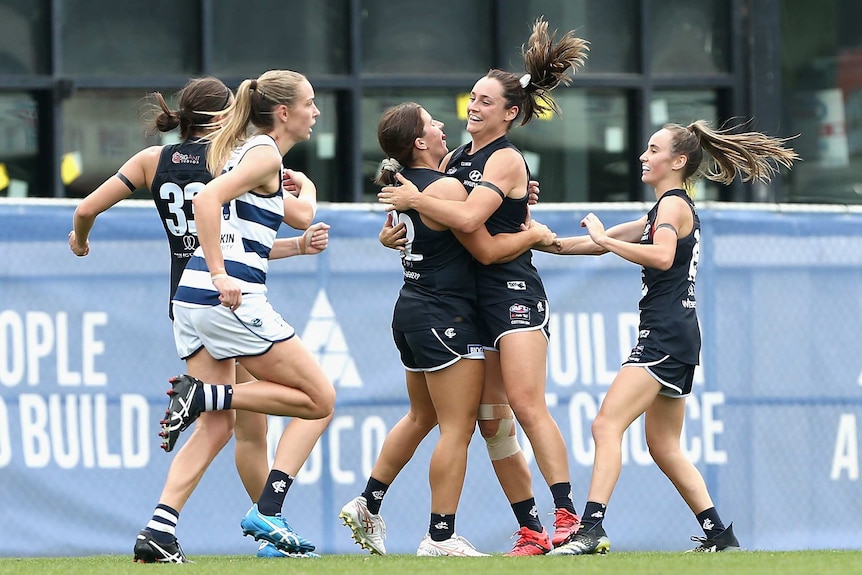 Carlton players celebrate by jumping and hugging as a Geelong player walks past