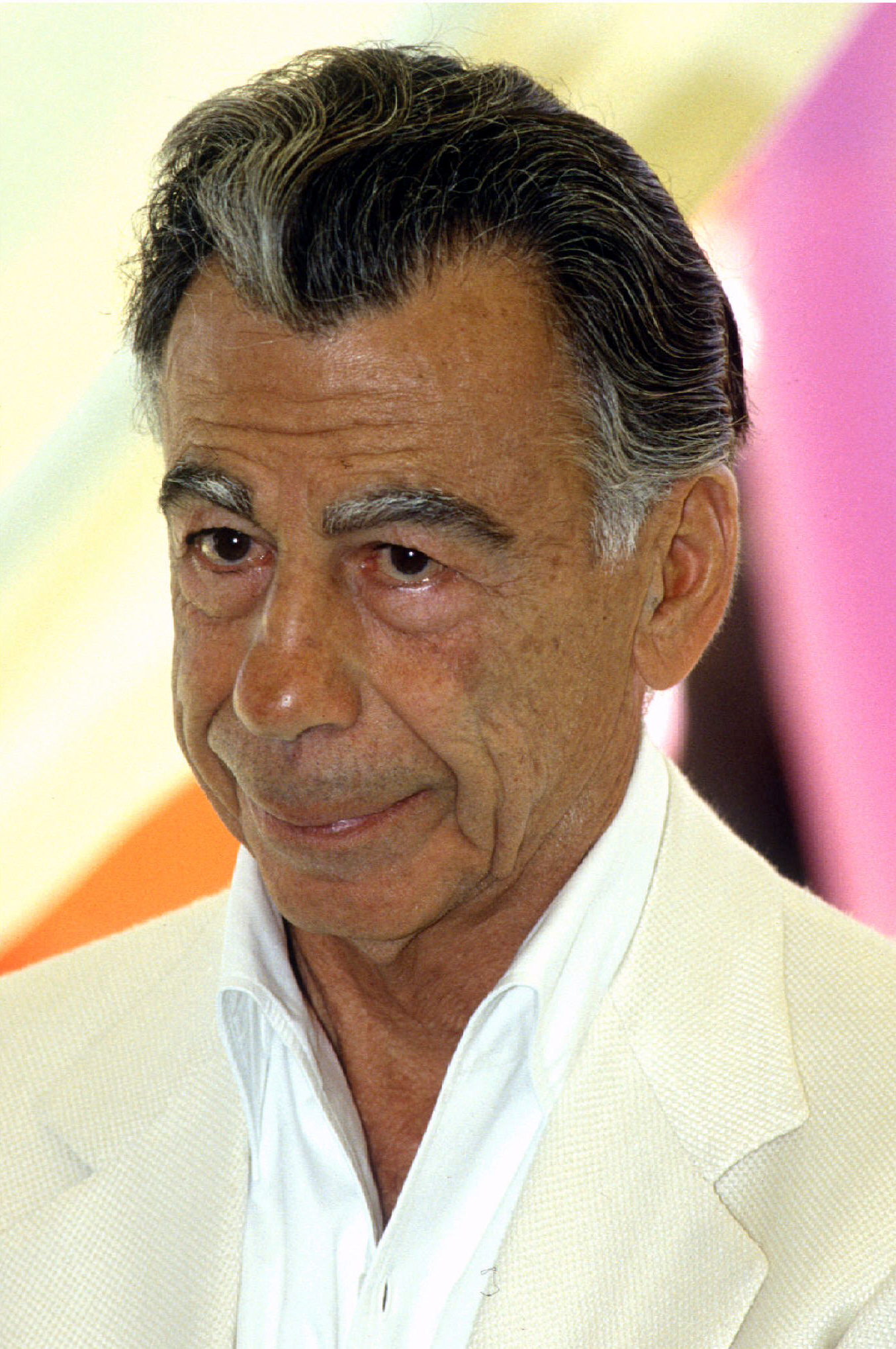 A grey haired man in  a cream coloured suit. 