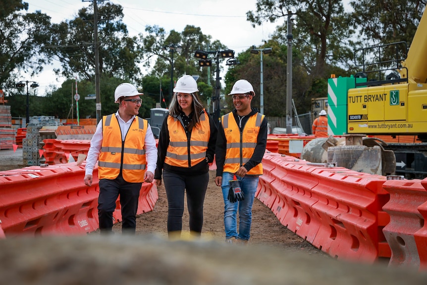 Two men and a woman wearing hard hats and hi vis smiling while walking through a construction site.