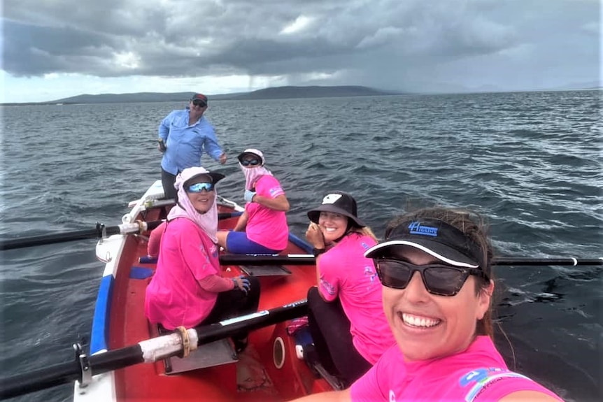Women in a row boat smile at the camera while at sea