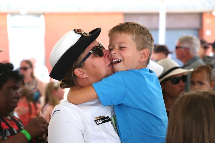 A servicewoman in uniform picks up her son and kisses him