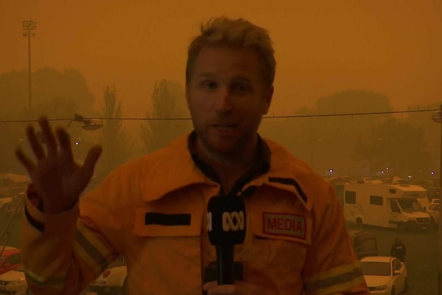 Macdonald holding a microphone with smoky orange background.