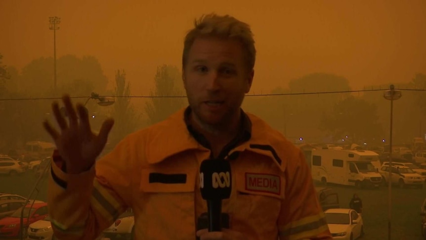 Macdonald holding a microphone with smoky orange background.