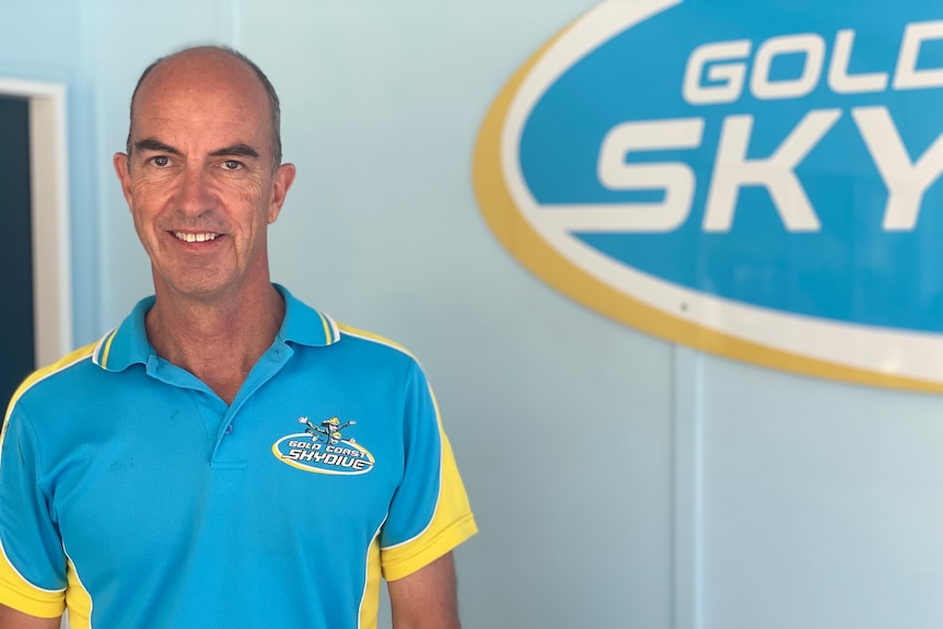 A man in a blue shirt smiles in front of a sign.