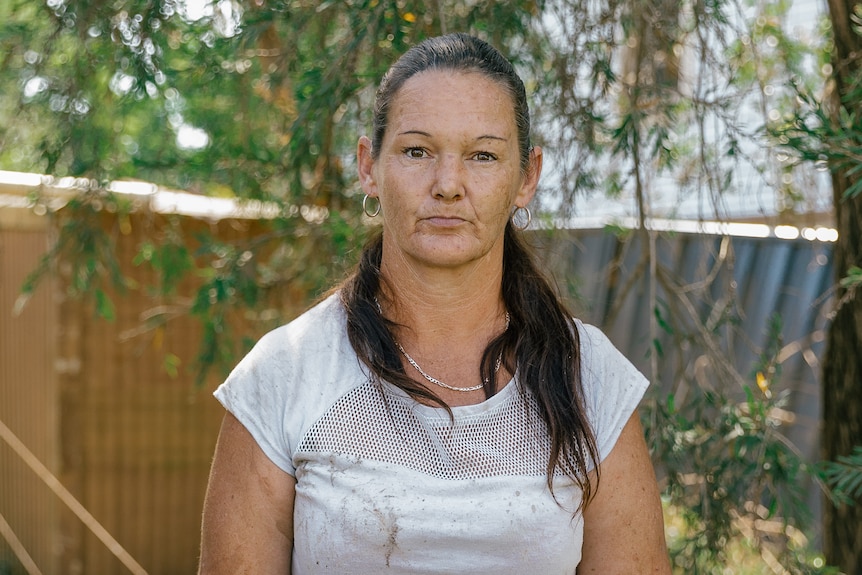 A woman with ponytail in gumboots holds broom surrounded by dirty yard