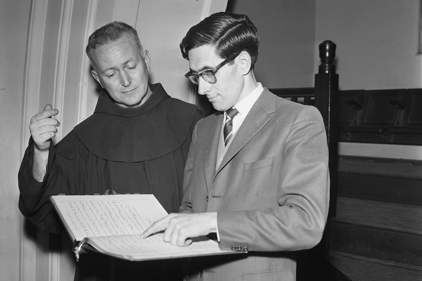 A black and white photo of two men looking at a musical composition book.
