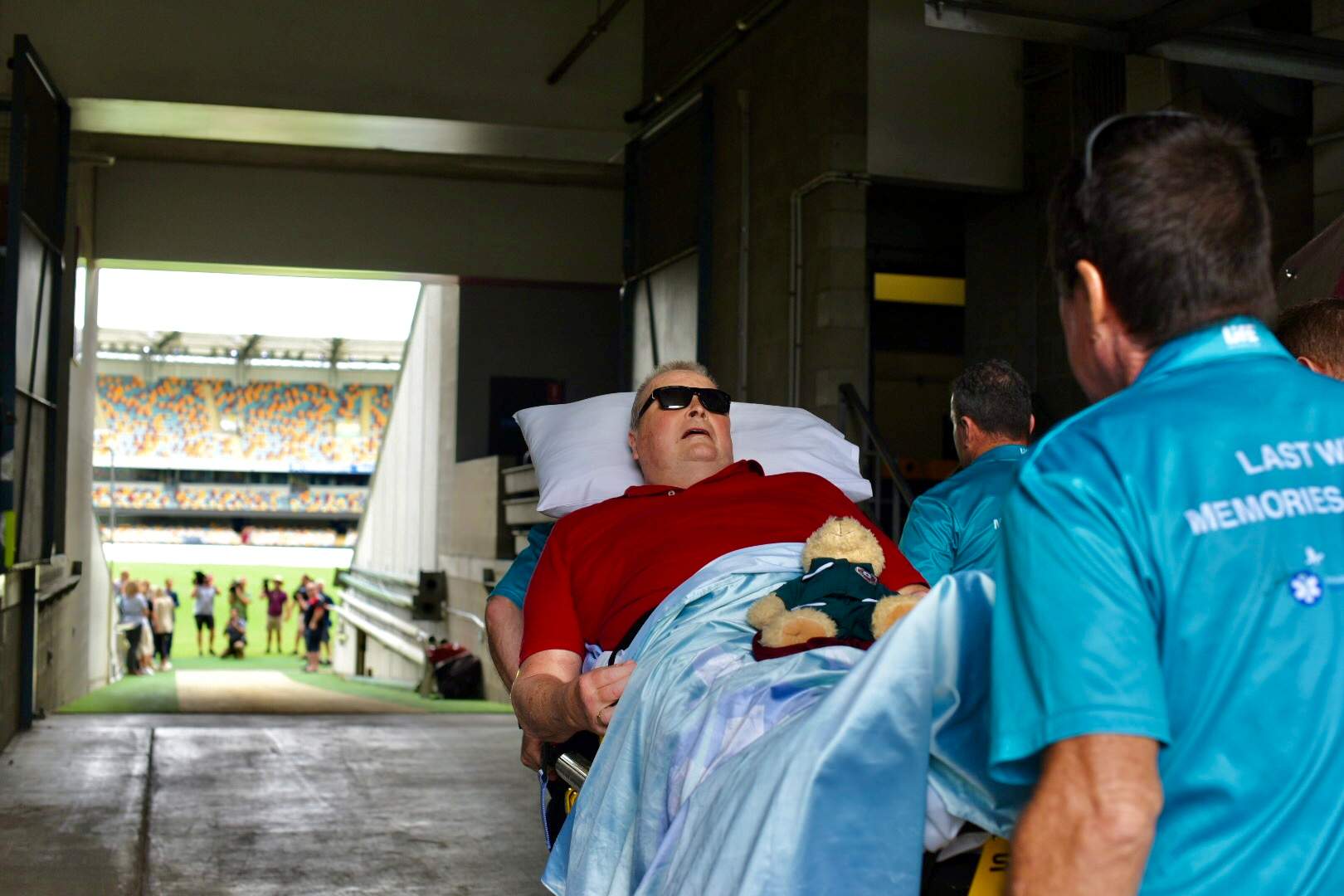 A man is wheeled into a stadium in a hospital bed.