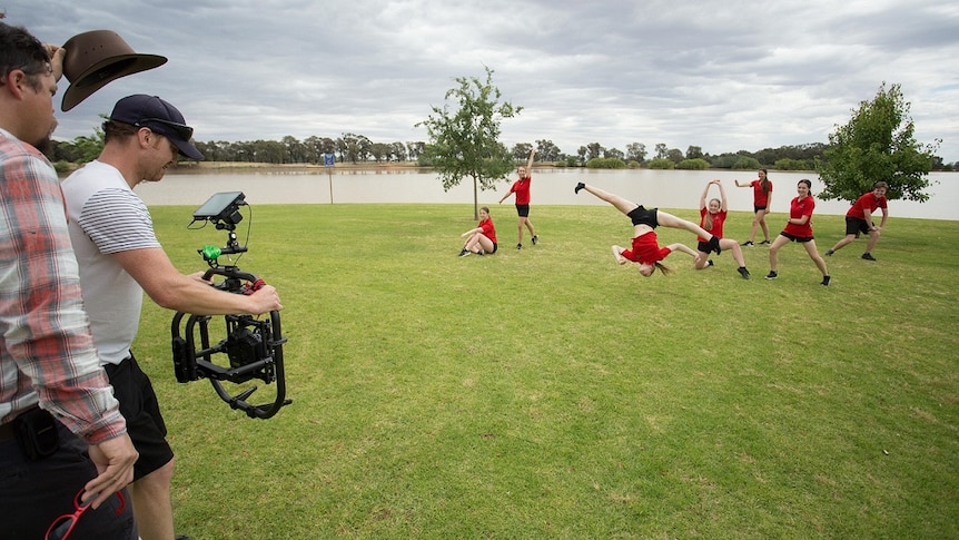 Young jazz dancers perform and do somersaults in a park by a lake