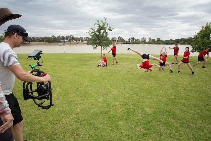 Young jazz dancers perform and do somersaults in a park by a lake