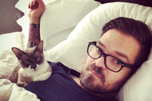 A man lies in bed with a cat resting on his chest, recovering from prostate cancer surgery.