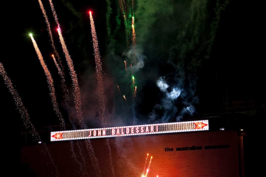 An illuminated sign on a building with fireworks exploding around it.