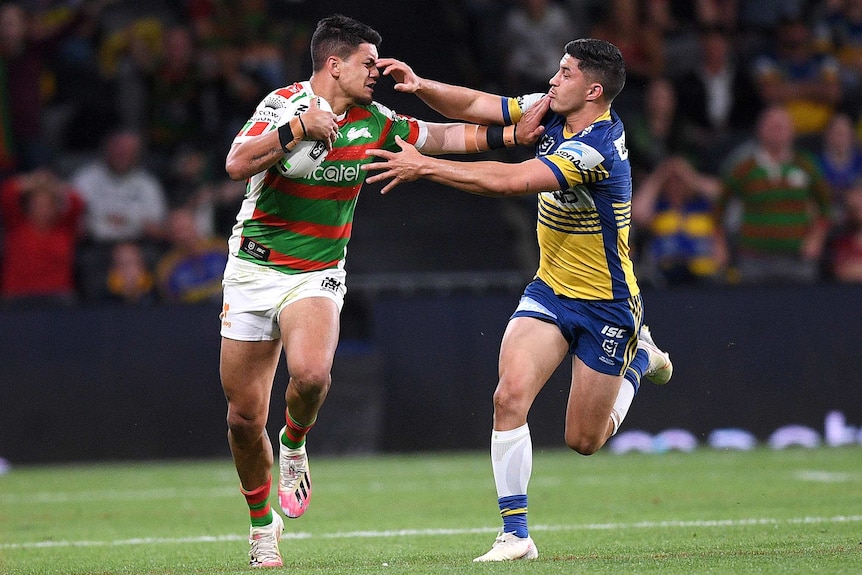 A South Sydney NRL player stretches out his right hand as he attempts to palm off a Parramatta opponent.