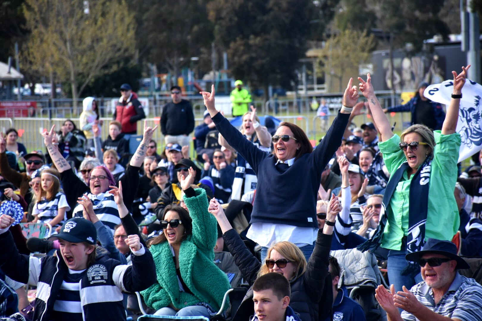 Fans dressed in blue and white cheer, stand and raise their arms after their team scored its first goal.