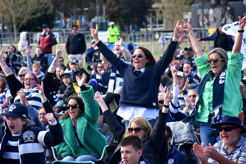 Fans dressed in blue and white cheer, stand and raise their arms after their team scored its first goal.