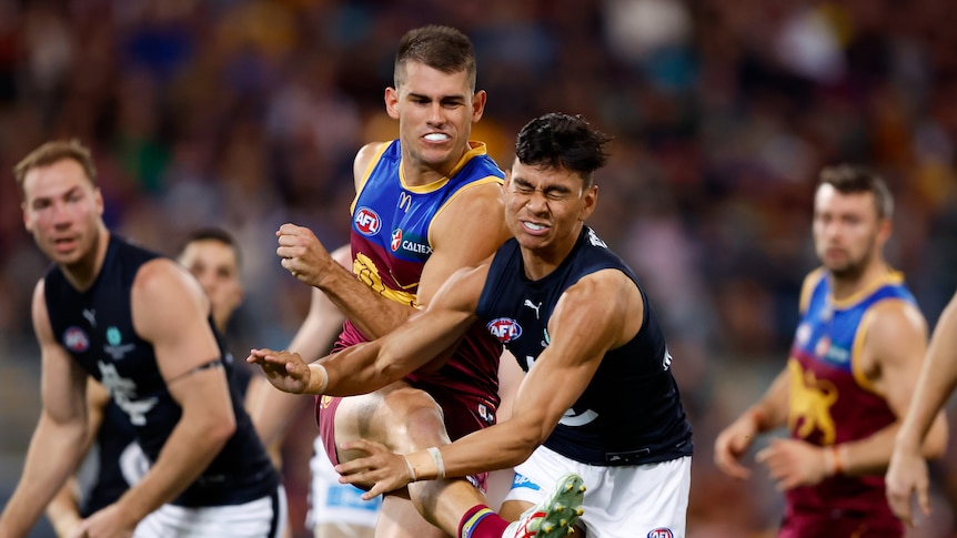 A Carlton defender grimaces as he tries to smother a kick from a Brisbane Lions player during a final.