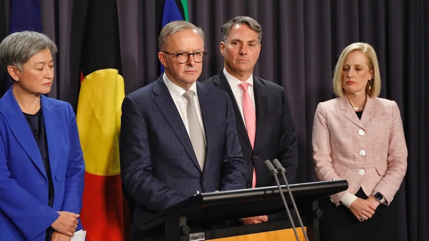 Prime Minister Anthony Albanese standing in front of Aboriginal and Torres Strait Islander flags.