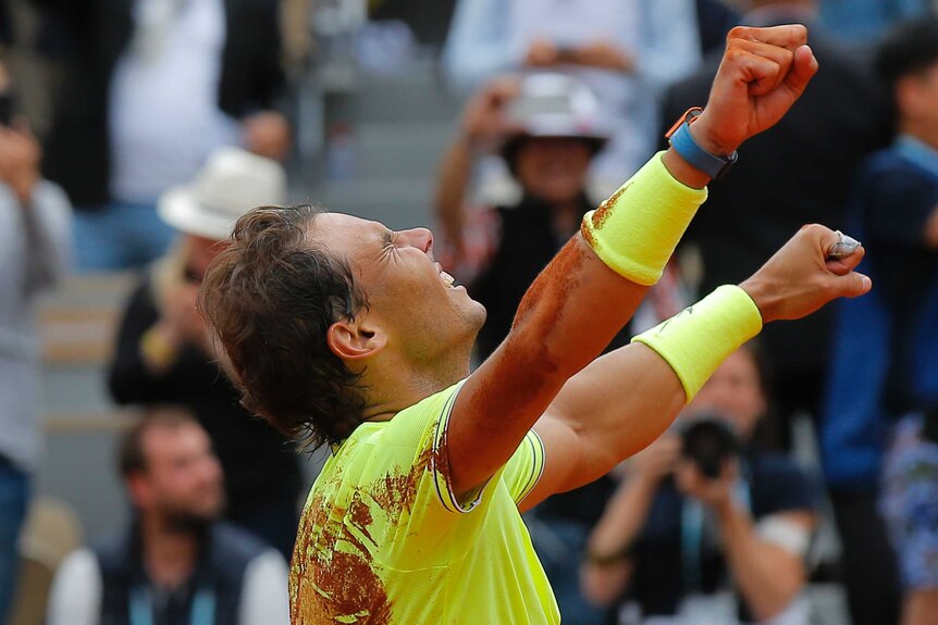 Rafael Nadal wears bright yellow shirt and wristbands and throws his arms in the air in celebration