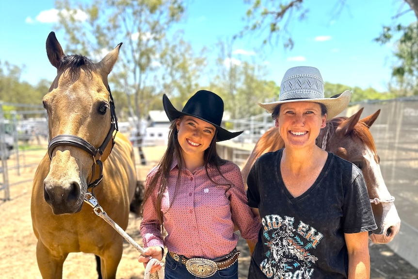 A cowgirl wearing a pink shirt and black hat and her mum wearing a white hat and black T shirt standing with two horses.