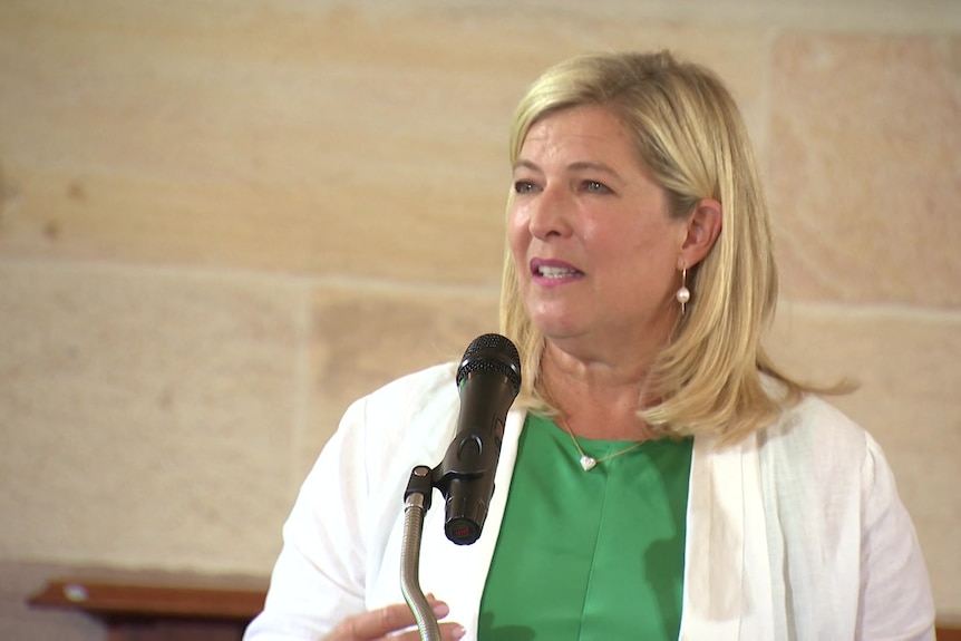 NSW minister bronnie taylor wearing white jacket, green top, speaks into a microphone.