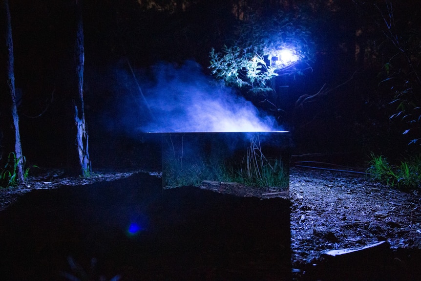 A bath clad in reflective material outside in the dark, steam rising off the water, this is artwork Flow State
