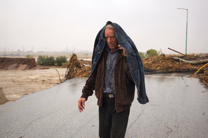 A man walks along a road with a jacket over his shoulders and head.
