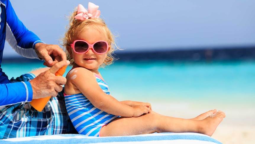 Father applies sunscreen to young daughter's shoulder