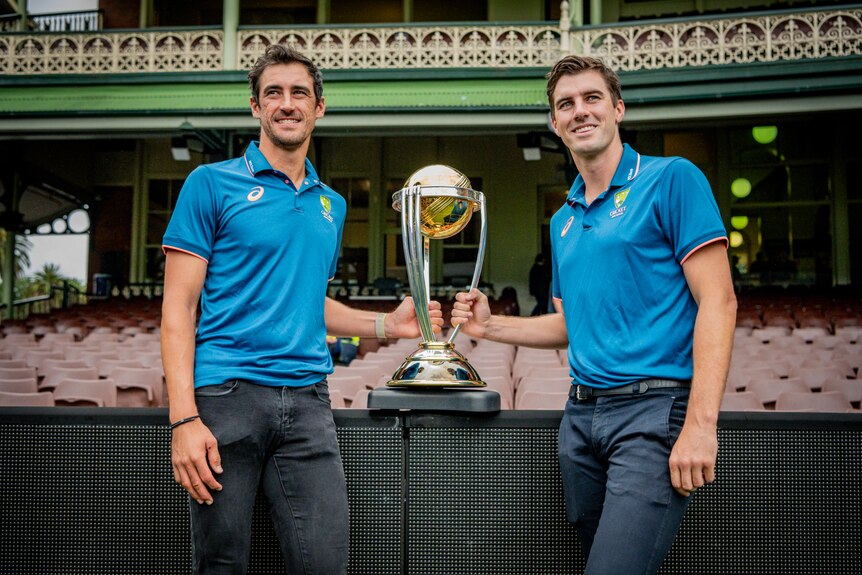 Mitchell Starc and Pat Cummins standing with the ICC World Cup trophy.
