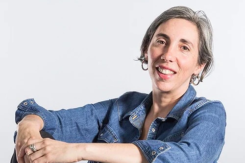 Associate Professor Jennifer Smith Merry, who has short dark hair, poses for a photo in a denim jacket and gold hoop earrings