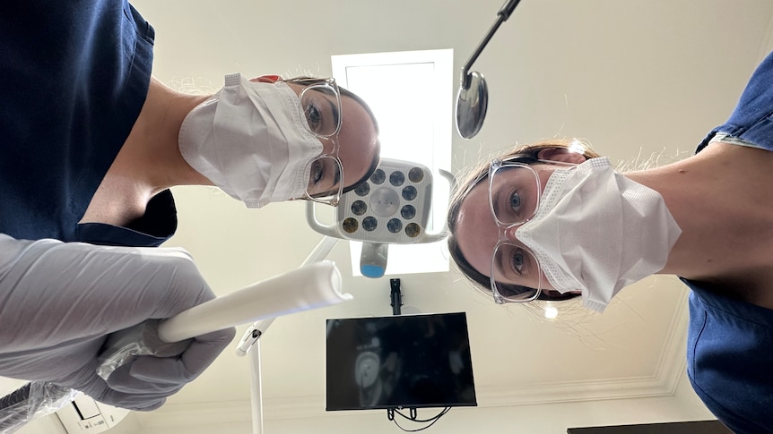 Two people wearing face masks and working with dental instruments.