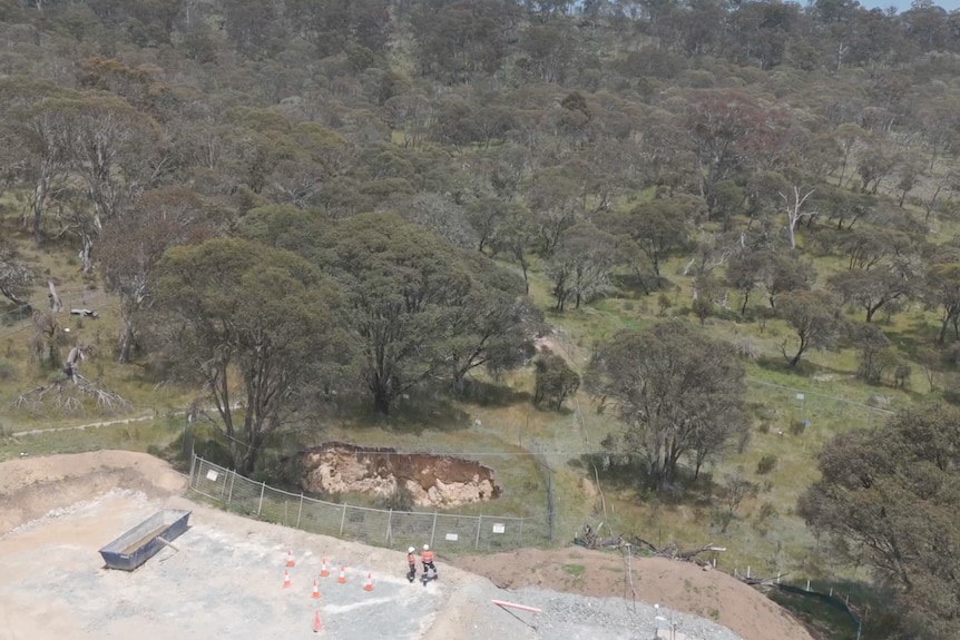 An aerial view of a hole surrounded by safety fencing in bushland.