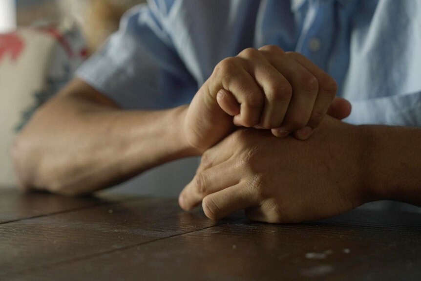 A teenage boy's hands on a table. He is fidgeting, wrapping fingers around his thumb.