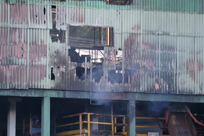 A close up of an old tin building with a hole burnt through it and smoke visible 
