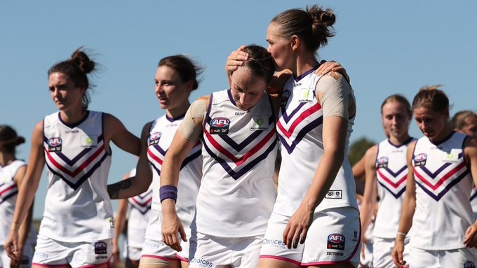 An AFLW player kisses her teammate's head and puts her arm around her after a finals loss.