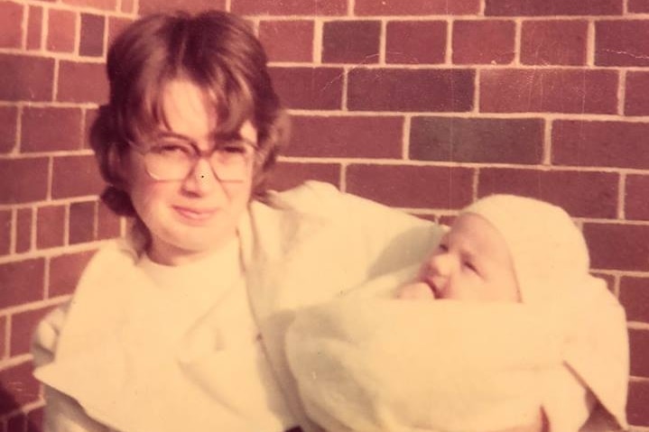 A woman with glasses holding a baby in an aged photograph with sepia tone