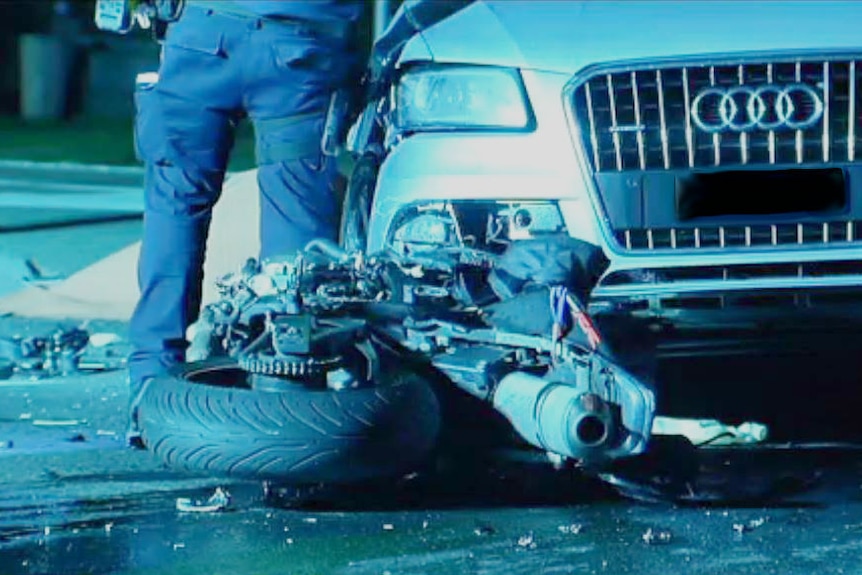 A wreck of a motorbike in front of an Audi car.