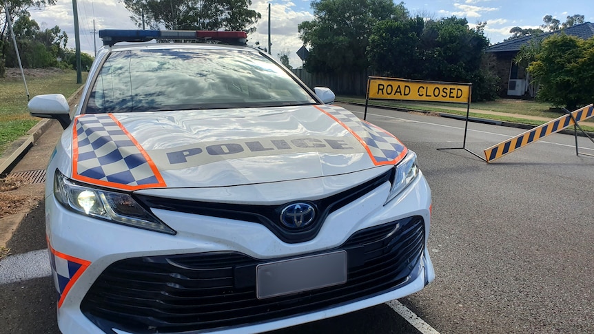 A police car on a road in front of a road closed sign.