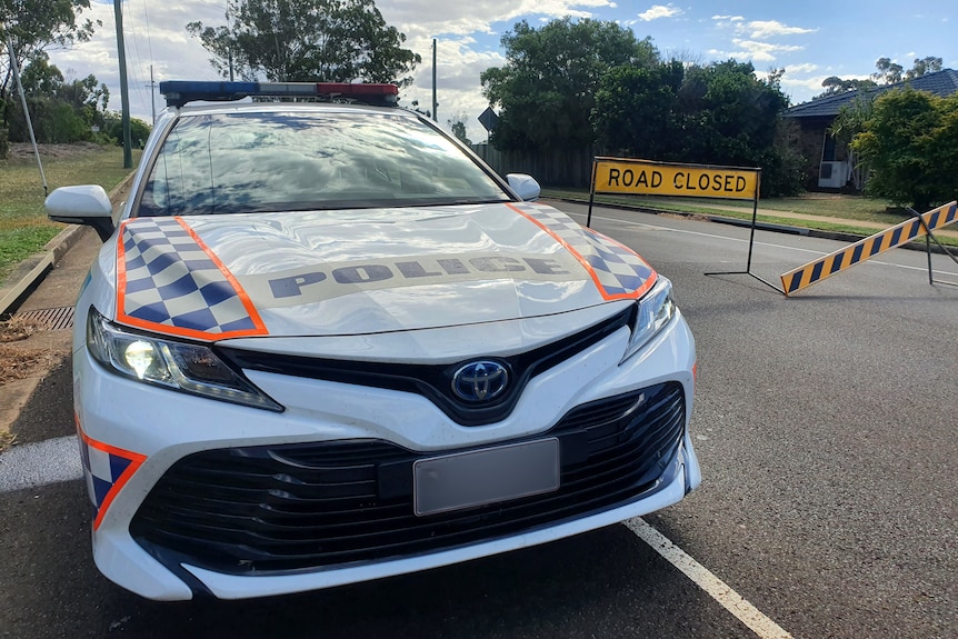 A police car on a road in front of a road closed sign.