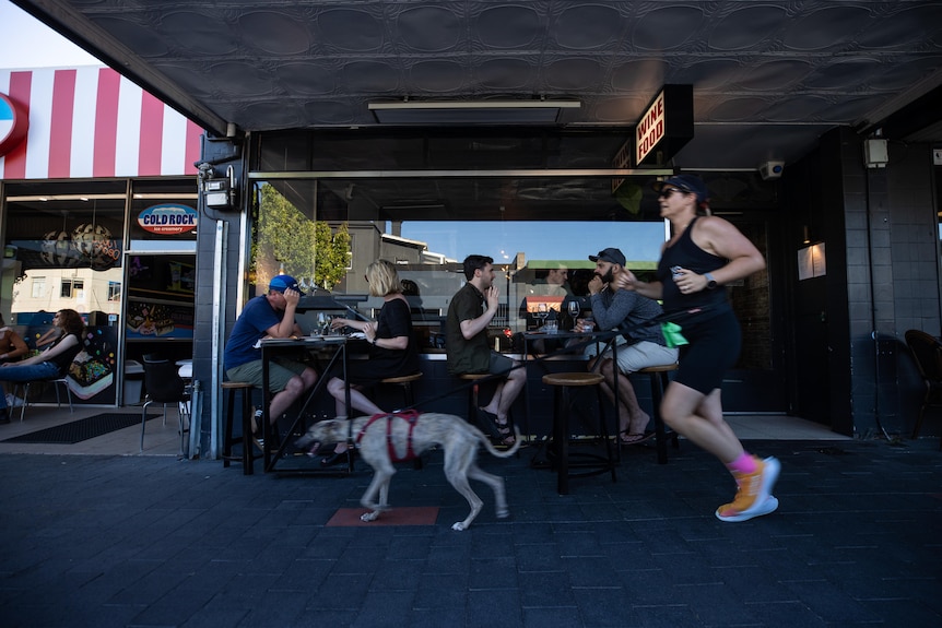 A woman and a dog run past a cafe.