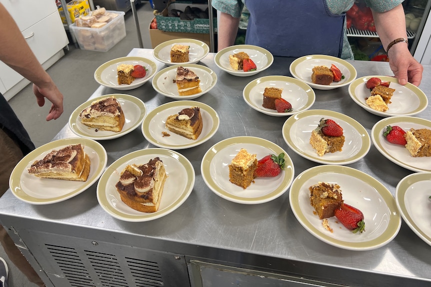 Plates of desert laid out on a stainless steel bench in a commercial kitchen.