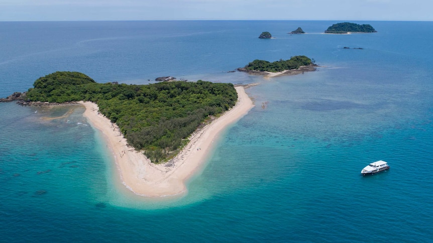An aerial view of a small island surround by ocean, with a boat on the right.