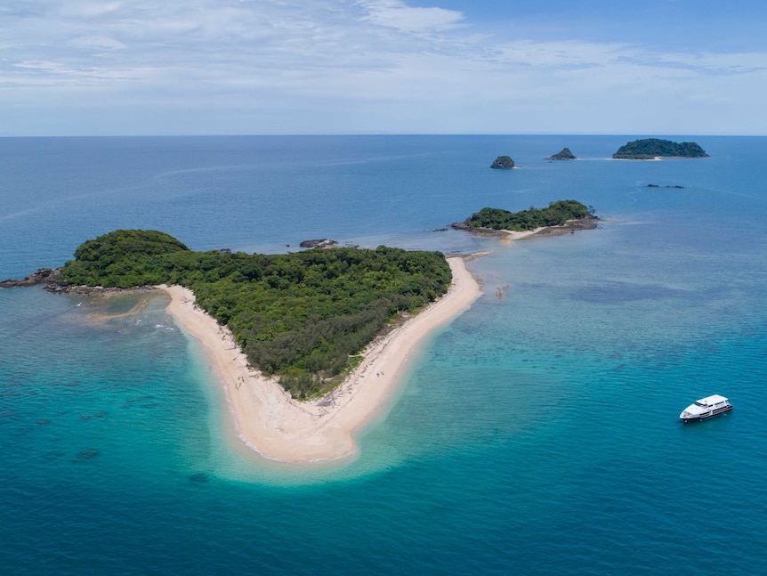 An aerial view of a small island surround by ocean, with a boat on the right.