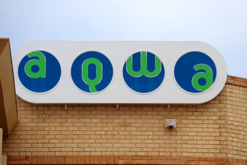 A white sign on a brick wall with blue circles in green letters that reads A Q W A.