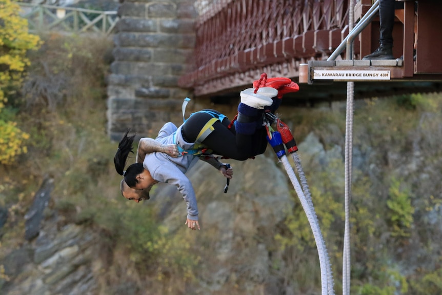 A woman and a man wearing safety kit hold each other as they fall from a bungee-jump platform.