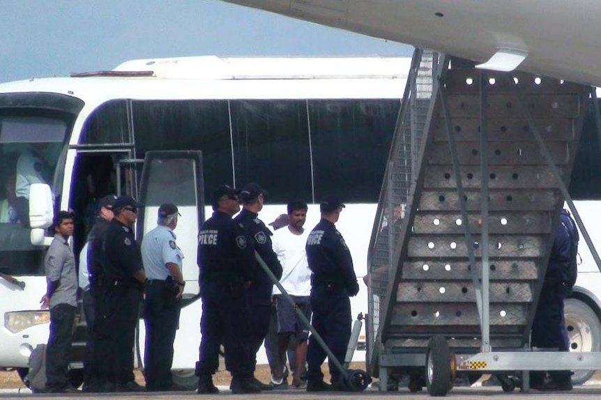 Asylum seekers board a plane on Christmas Island under police presence.