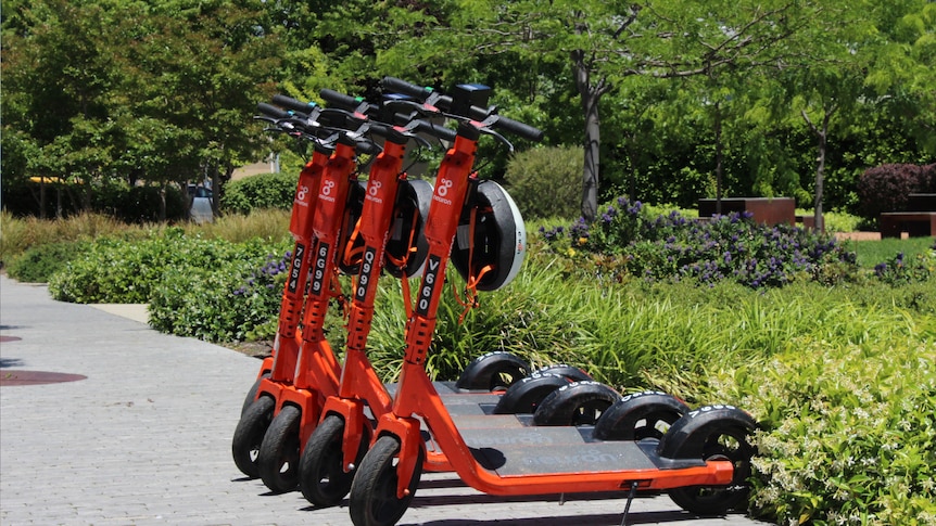 Four orange scooters with white helmets on them lined up