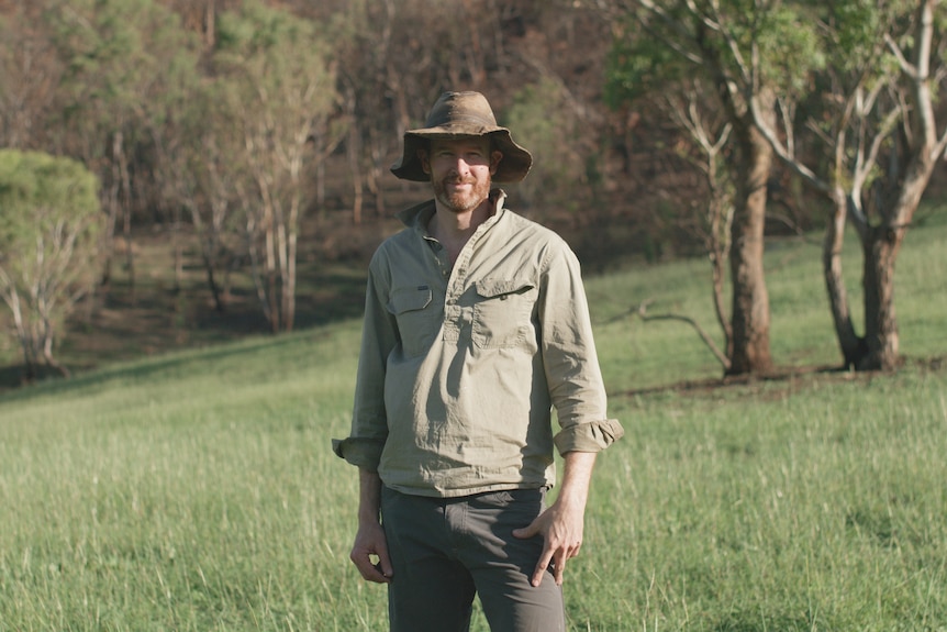 A man in a hat and outdoor gear stands in a paddock.